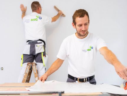 Zwei Mitarbeiter der HSG tapezieren die Wände